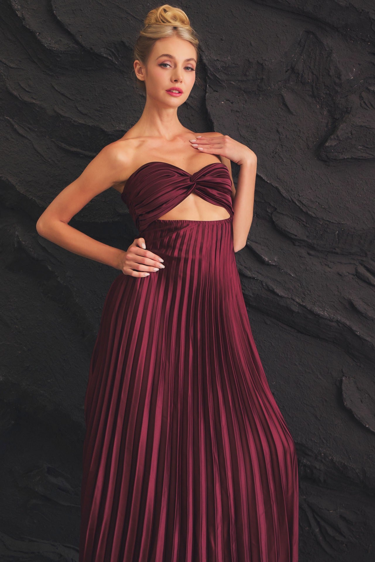 Burgundy strapless dress featuring a twist-front bodice and flowy pleated skirt, perfect for formal events and elegant celebrations.