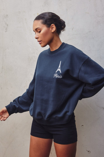 Model showcasing an oversized travel-inspired sweatshirt with embroidery in Brown and Navy colors, ideal for casual wear.