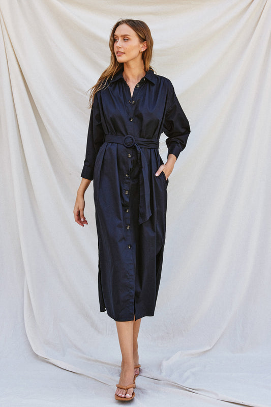 Navy poplin midi dress with a collared neckline, tortoise buckled belt, long sleeves, and side pockets, styled for work or fall gatherings.