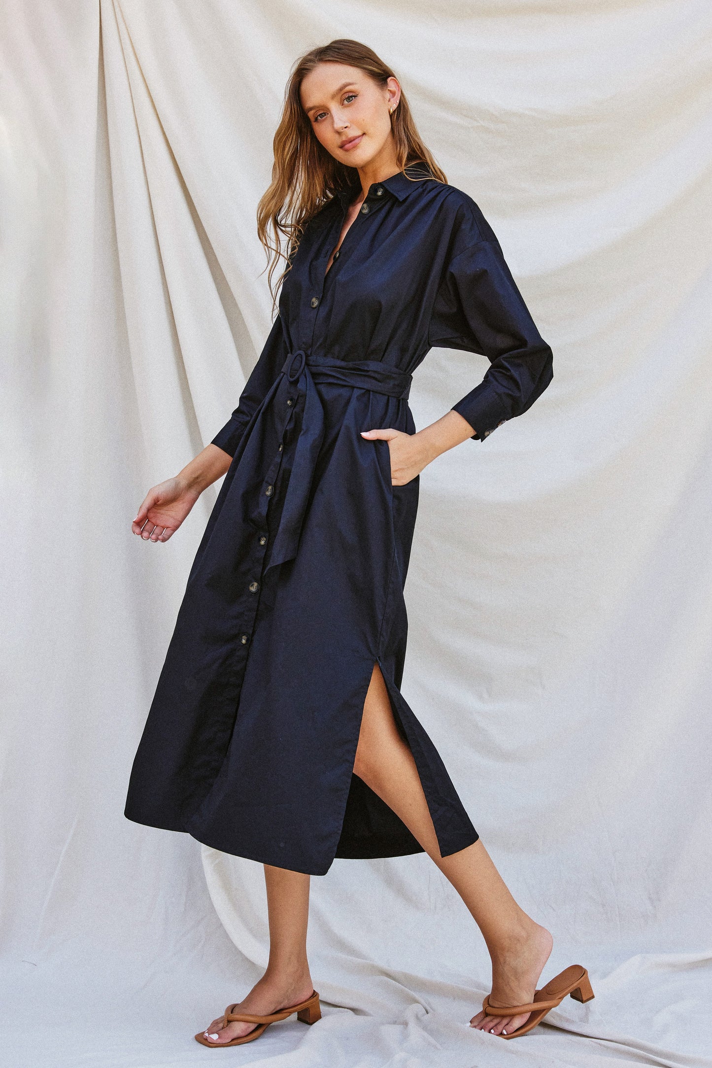 Navy poplin midi dress with a collared neckline, tortoise buckled belt, long sleeves, and side pockets, styled for work or fall gatherings.