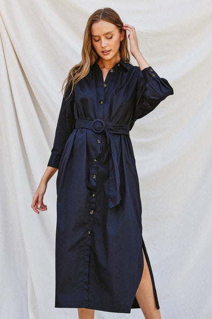 Navy poplin midi dress with a collared neckline, tortoise buckled belt, long sleeves, and side pockets, styled for work or fall gatherings.