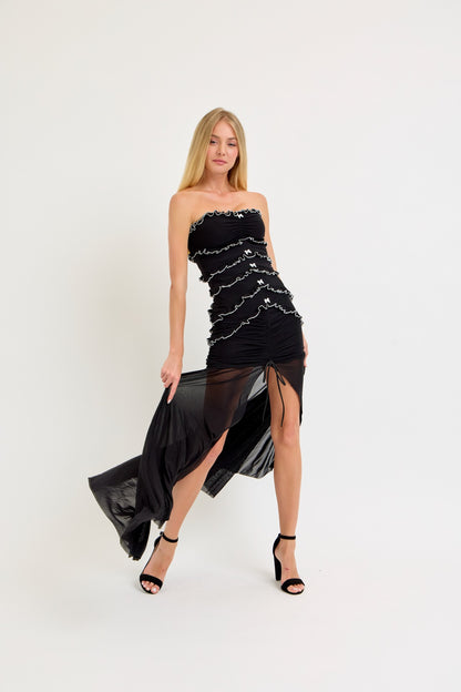 Strapless black maxi dress with ruffle and bow details, featuring a bodycon fit and a sheer mesh skirt, ideal for birthdays and evening events.